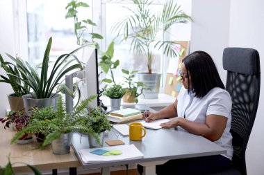Black Office Female Sitting At Desk Working On Laptop Taking Notes At Work Indoor. Business Schedule Concept. Attractive Lady in White Shirt Concentrated On Work. In cozy modern office