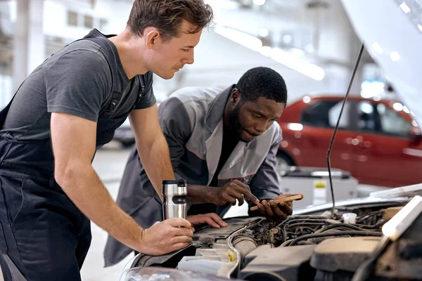diverse Caucasian and black Men mechanic inspection checking bug in engine from application smartphone. white car for service maintenance insurance with car engine.for transport automobile automotive