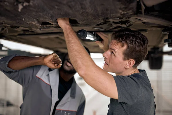 Car service with mechanical team for check suspension of SUV car using Lamp, Diverse Black And Caucasian Auto mechanics repair car,service via insurance system at modern clean garage