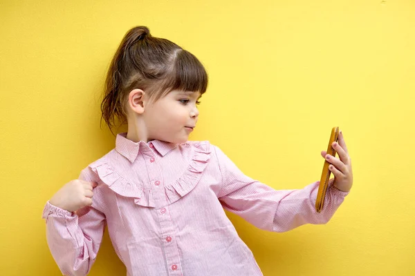 portrait of child girl taking photo or making video on smartphone, posing at phones camera. Adorable little girl in pink blouse using modern technologies. Children and human lifestyle concept