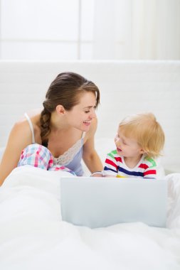 genç anne ve bebek yatakta dizüstü bilgisayar ile oynamak
