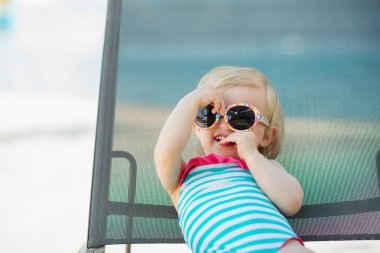 Portrait of baby in swimsuit and sunglasses laying on sunbed clipart