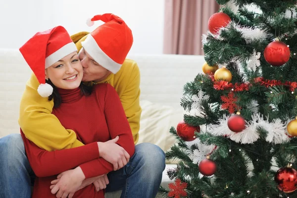 Young man kissing girlfriend near Christmas tree — Stock Photo, Image