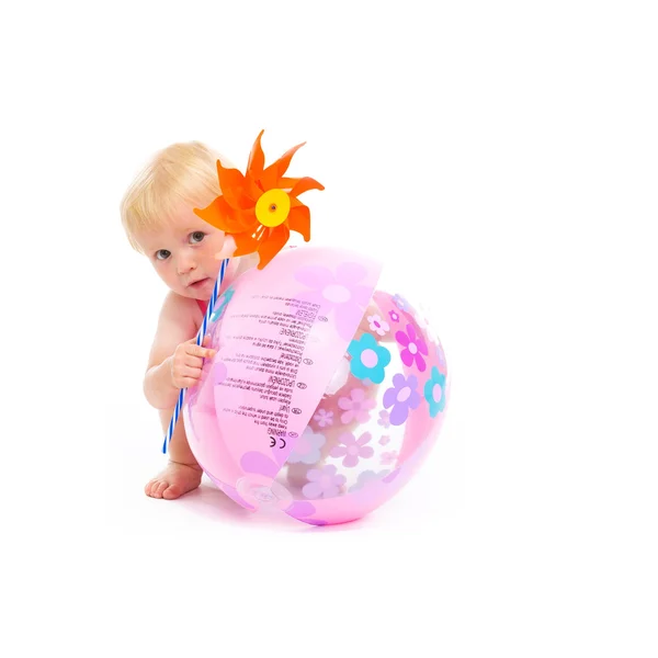 Baby in swimsuit with pinwheel hiding behind beach ball — Stock Photo, Image