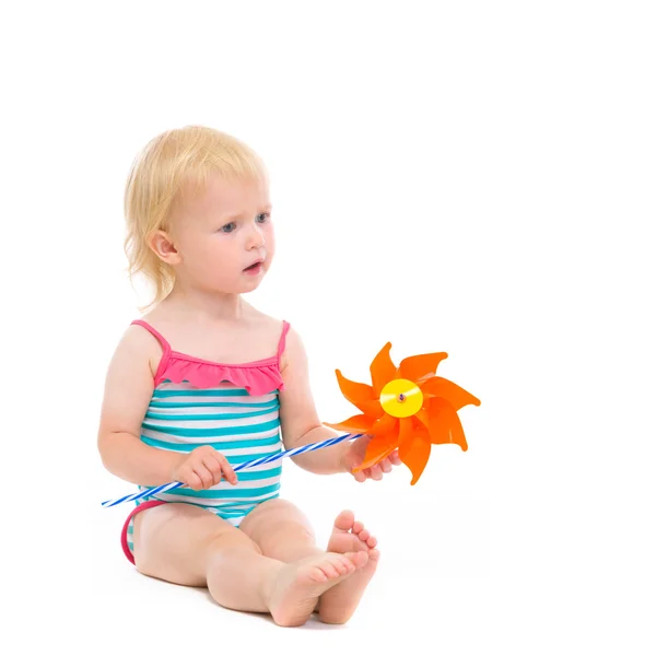 Thoughtful baby in swimsuit with pinwheel sitting on floor — Stock Photo, Image