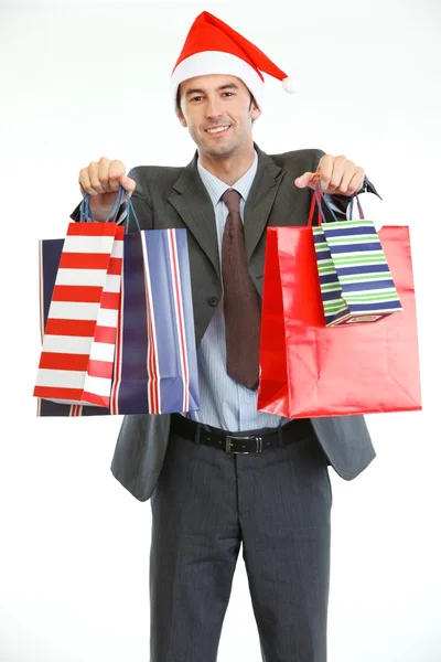 Homem de negócios sorridente no chapéu do Papai Noel mostrando sacos de compras — Fotografia de Stock