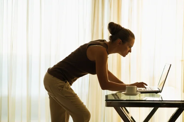 Νεαρή γυναίκα χρησιμοποιώντας φορητό υπολογιστή που ακουμπάει πίνακα — Φωτογραφία Αρχείου