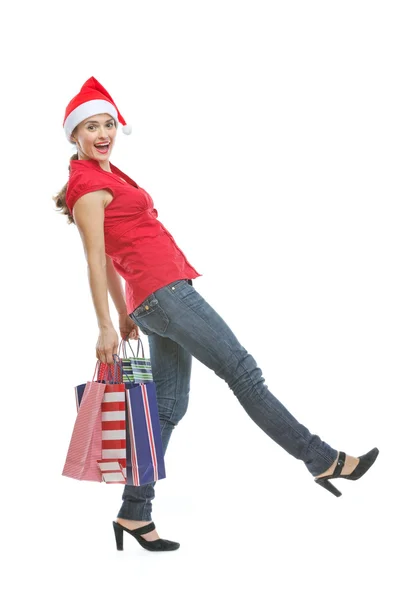 Mulher feliz no chapéu de Natal com sacos de compras fazendo passo — Fotografia de Stock