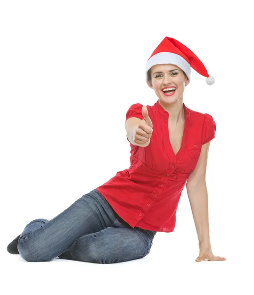 Glückliche Frau mit Weihnachtsmütze sitzt auf dem Boden und zeigt Daumen — Stockfoto