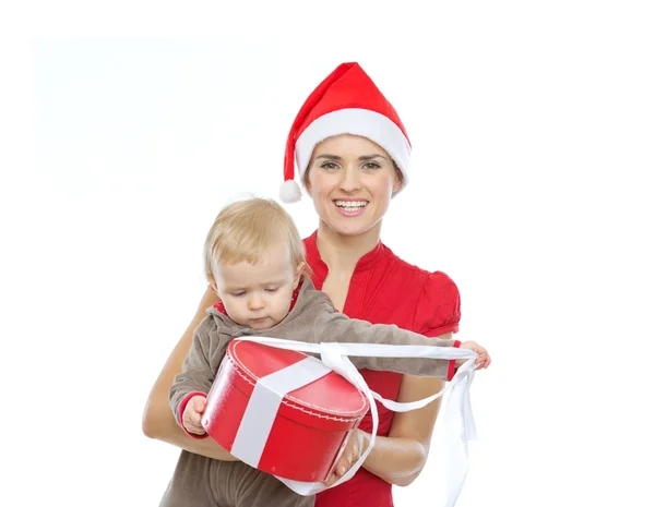 Mãe no chapéu do Papai Noel segurando bebê abrindo presente de Natal — Fotografia de Stock