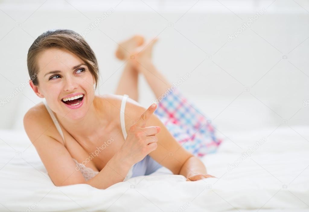 Happy woman laying on bed and pointing on copy space