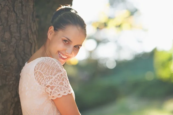 Sonriente joven mujer se inclinan contra el árbol —  Fotos de Stock