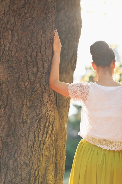 Mujer joven apoyada contra el árbol. Vista trasera — Foto de Stock