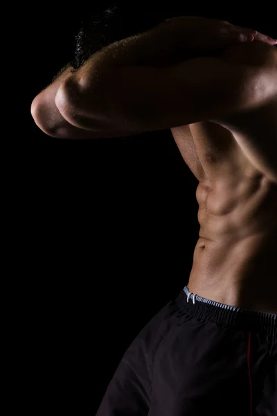 Strong muscular athlete showing abdominal muscles on black — Stock Photo, Image