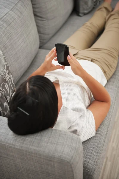 Giovane donna che gioca sul divano con il telefono cellulare — Foto Stock