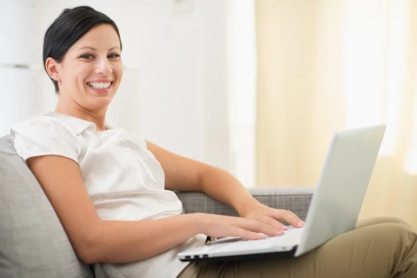 Uśmiechnięta młoda kobieta surfing netto na laptopie w salonie — Zdjęcie stockowe