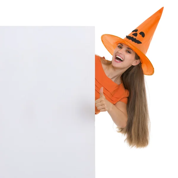 Femme heureuse dans le chapeau d'Halloween montrant panneau d'affichage vierge et pouces — Photo