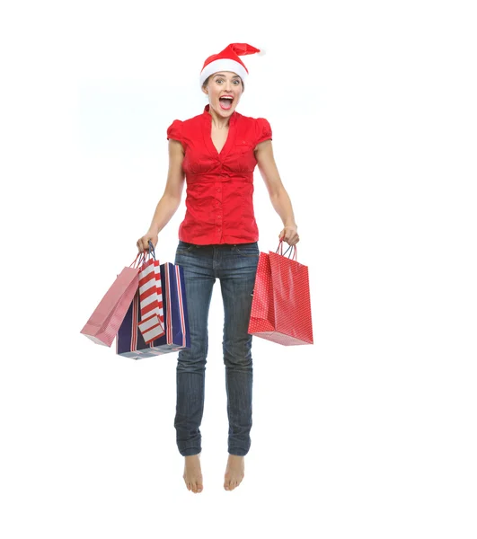 Happy young woman in Christmas hat with shopping bags jumping — Stock Photo, Image