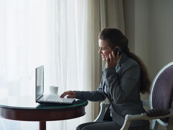 Mujer de negocios trabajando en el ordenador portátil y hablando móvil en el hotel ro —  Fotos de Stock