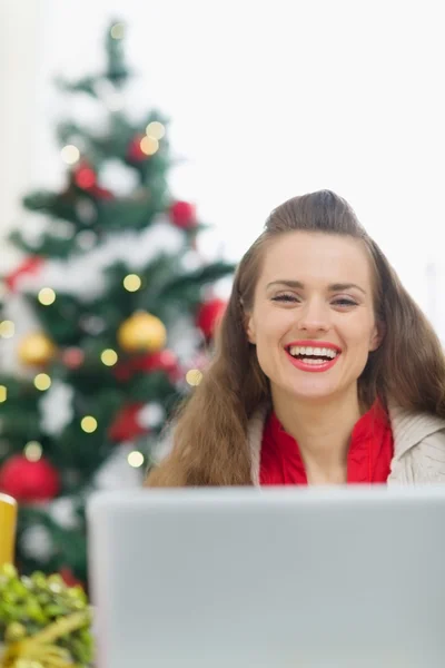 Glad ung kvinna nära julgran med laptop — Stockfoto