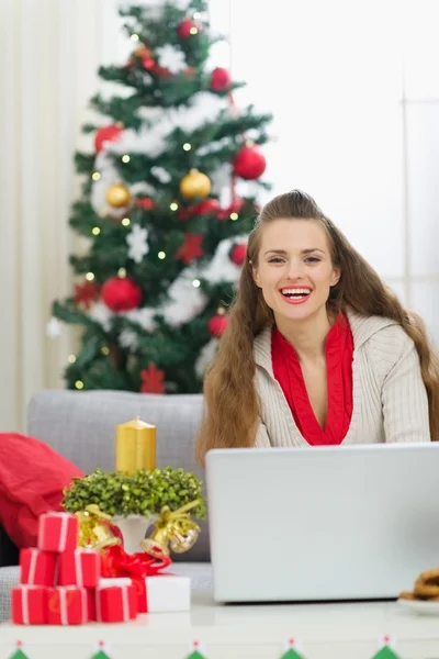 Χαμογελώντας νεαρή γυναίκα κοντά χριστουγεννιάτικο δέντρο αποστολή ευχετήριων μηνυμάτων ηλεκτρονικού ταχυδρομείου — Φωτογραφία Αρχείου