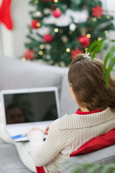 Egy nő laptopot használ a karácsonyfa közelében. Hátsó nézet — Stock Fotó