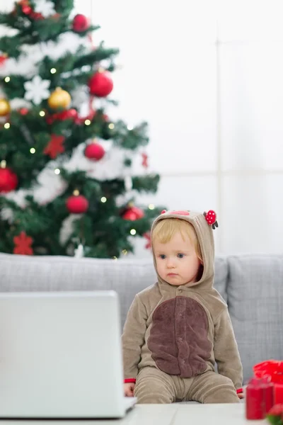 Baby in Christmas deer costume near Christmas tree looking in la — Stock Photo, Image