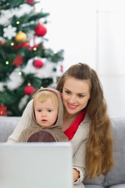 Madre y bebé cerca del árbol de Navidad con el ordenador portátil —  Fotos de Stock