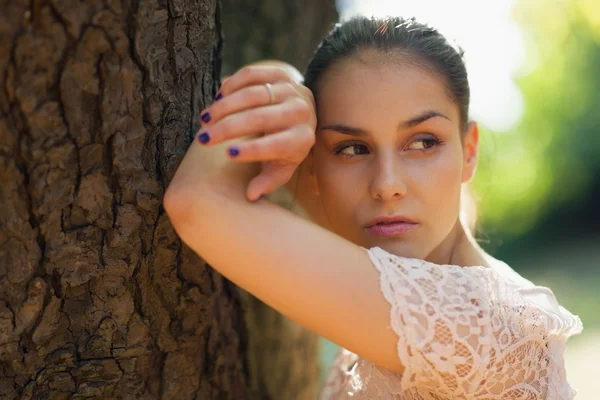 Thoughtful young woman lean against tree Stock Photo