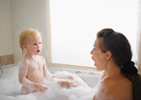 Surprised mother and baby in foam filled bathtub — Stock Photo, Image