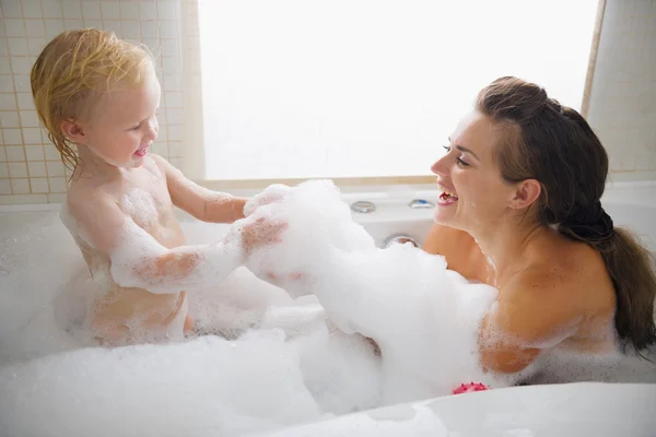 Moeder en baby spelen met schuim in badkuip — Stockfoto
