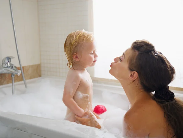 Baby kissing mother while washing in foam filled bathtub — Stock Photo, Image