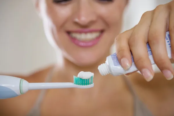 Gros plan sur les mains serrant le dentifrice sur la brosse à dents électrique — Photo