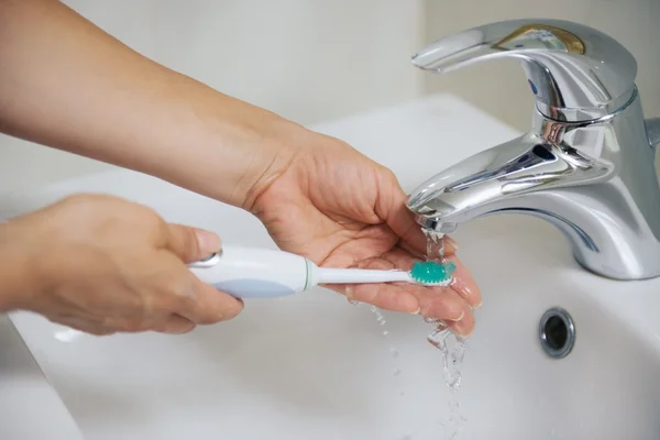 Primer plano en el lavado de manos cepillo de dientes eléctrico bajo corriente de agua — Foto de Stock