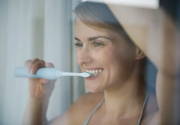 Mujer joven cepillándose los dientes con cepillo de dientes eléctrico y buscando — Foto de Stock