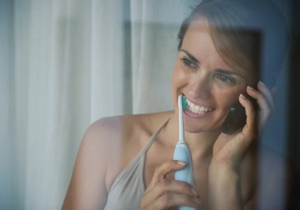 Mulher escovando dentes com escova de dentes elétrica e falando mobil — Fotografia de Stock