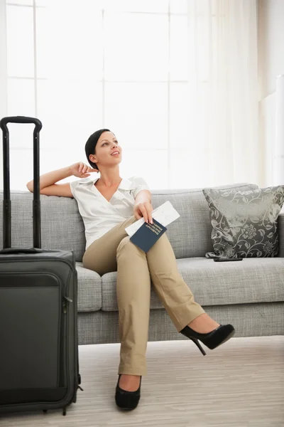 Мечтающая женщина с паспортом и авиабилетом сидит на диване — стоковое фото