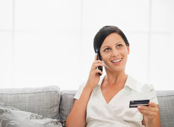 Happy young woman with credit card and speaking mobile phone — Stock Photo, Image
