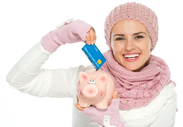 Donna felice in maglia abbigliamento invernale mettendo carta di credito nel maialino — Foto Stock