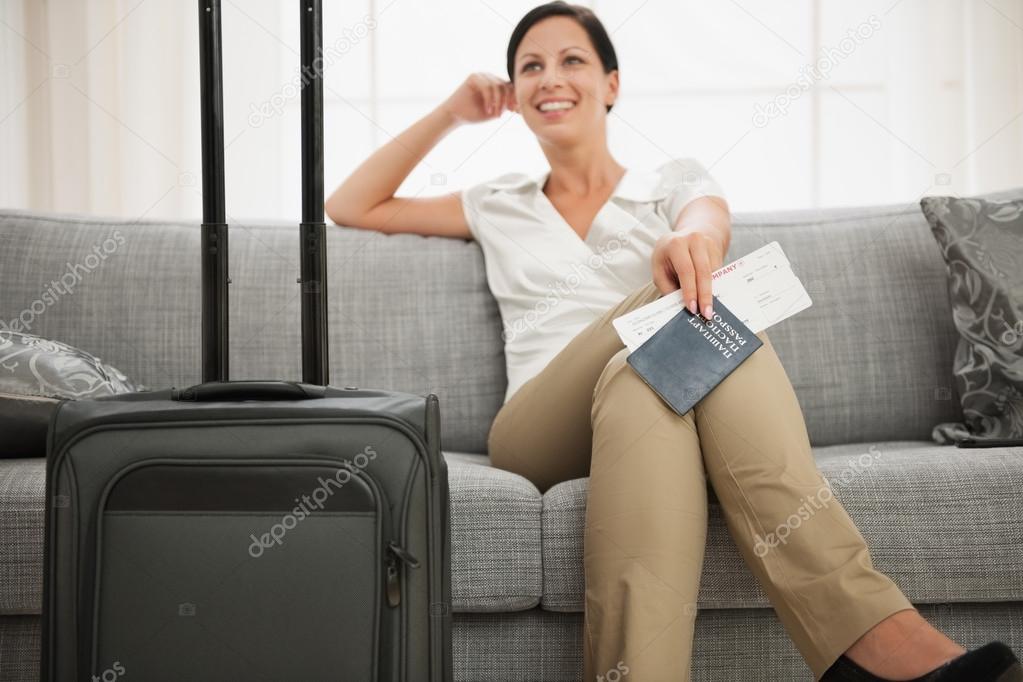 Dreaming woman with passport and air ticket sitting on couch