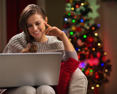 Mutlu kadın Noel ağacının önünde dizüstü bilgisayara bakıyor.