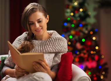 kadın kitap okuma Noel ağacı önünde sandalyede