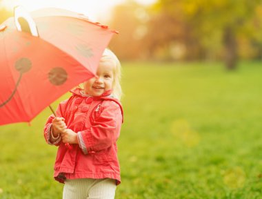 Smiling baby looking out from red umbrella clipart