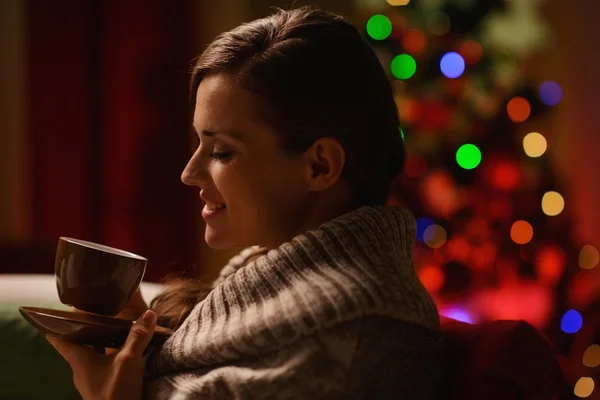 Happy woman sitting chair and drinking hot beverage in front of — Stock Photo, Image