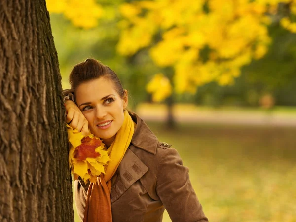 Femme réfléchie avec des feuilles tombées appuyées contre l'arbre — Photo