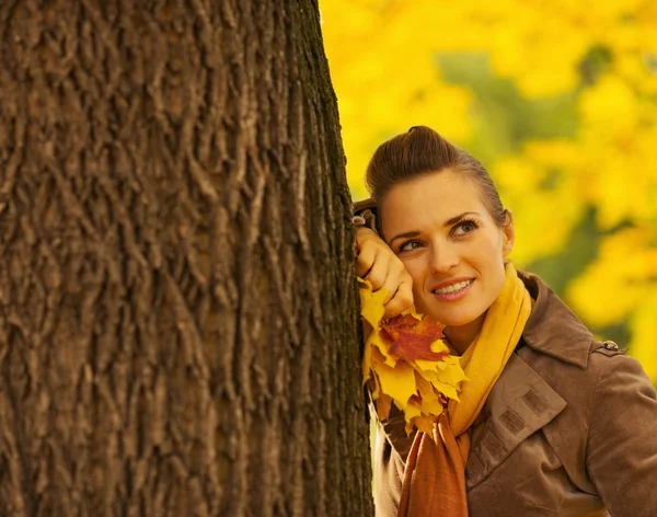 Dreaming woman with fallen leaves leaning against tree — Stock Photo, Image