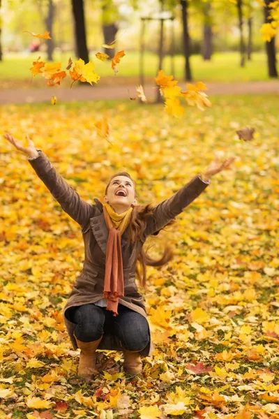 Happy woman squatting and throwing fallen leaves — Stock Photo, Image