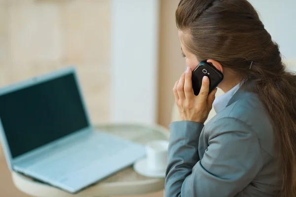 Biznes kobieta mówiąc, mobilnych i patrząc w laptopie. widok z tyłu — Zdjęcie stockowe