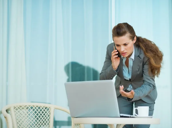 Besorgte Geschäftsfrau spricht Handy und schaut in Laptop — Stockfoto