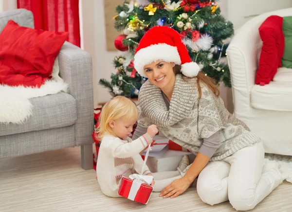 Baby sitzt neben Mutter und öffnet Weihnachtsgeschenkbox — Stockfoto
